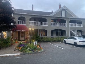 Two-story beige lodge with white railings and arched porches in Acadia National Park, pumpkins and flowers by the entrance.