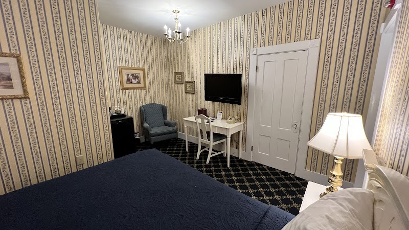 Cozy guest room with blue bedspread, striped wallpaper, chandelier, desk and chair, wall TV in Acadia National Park area.