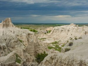 White Badlands spires along Notch Trail overlook in Badlands National Park, with eroded cliffs and distant hikers.