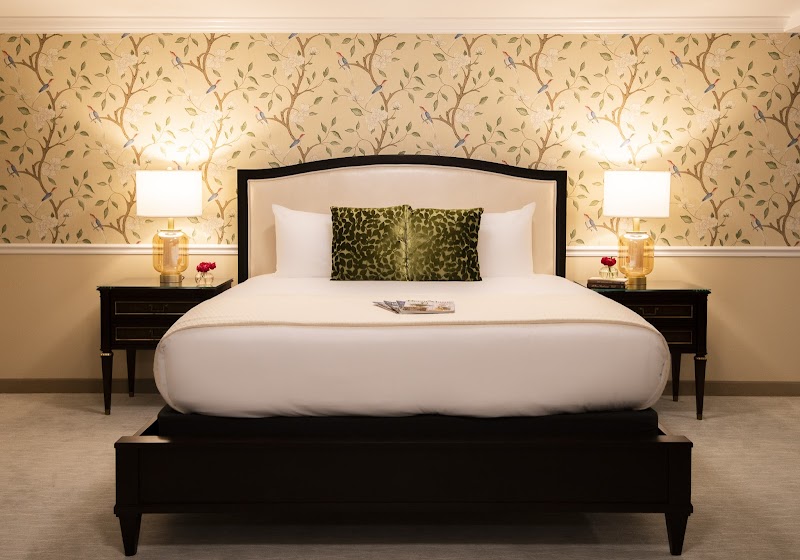 Luxurious hotel room with a king bed, two nightstands with lamps, floral wallpaper, and green patterned pillows in Acadia National Park.