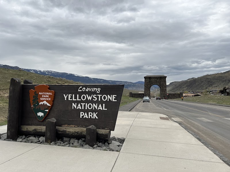 View along the road toward Roosevelt Arch in Yellowstone National Park, with a wooden Leaving sign and distant mountains.