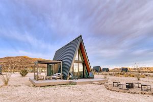 Stardust Big Bend lodging cabin, an A-frame retreat with glass walls, sits on desert terrain in Big Bend National Park.