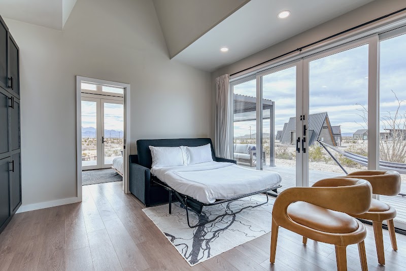 Interior of a contemporary lodging suite at Big Bend National Park, with a king bed, seating area, vaulted ceiling, and large glass doors to desert views.