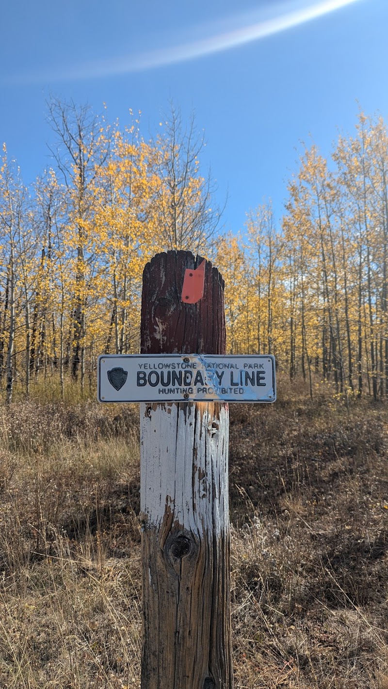 Yellowstone National Park boundary post with a weathered wooden stake and metal sign, autumn trees behind.