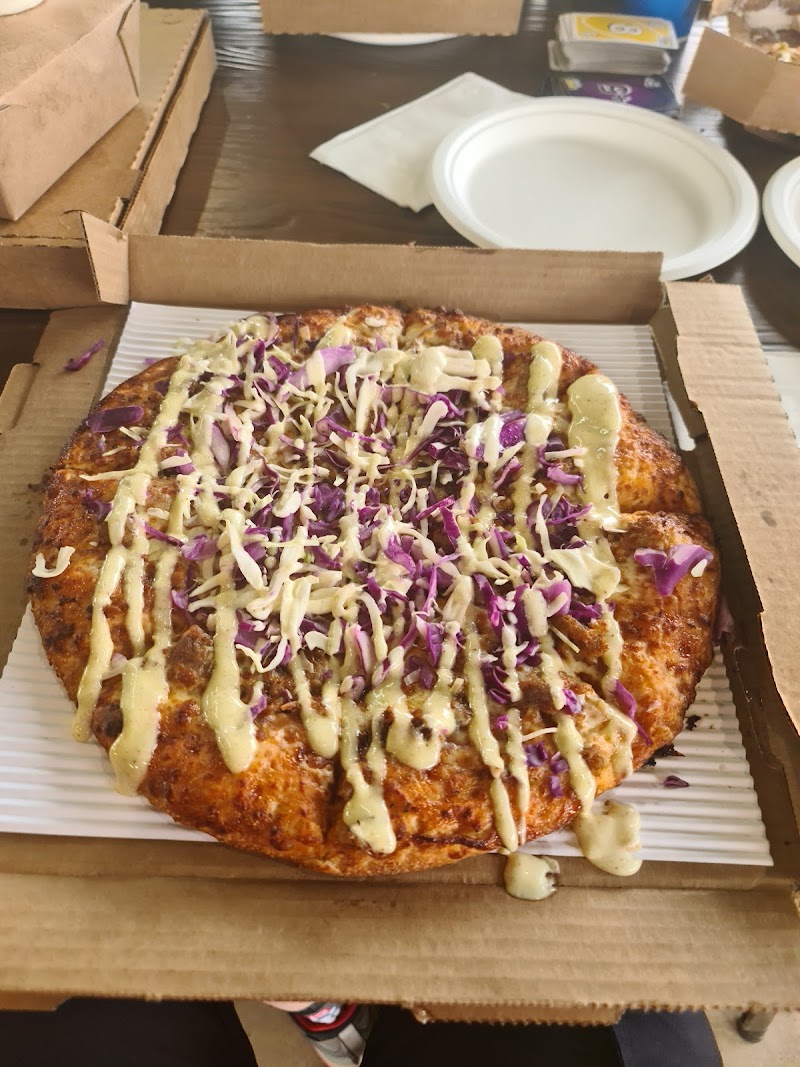 Pizza topped with purple cabbage and creamy drizzle sits in an open box on a table with plates in the background, Arches National Park