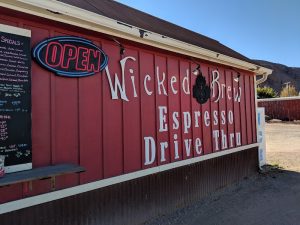 Red wooden cafe with a neon OPEN sign, chalkboard specials, and a drive-thru espresso window at Arches National Park.