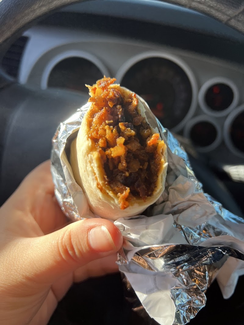 Close-up of a bite-sized beef taco wrap with melted cheese inside foil, held in a car with dashboard gauges visible, Arches National Park.