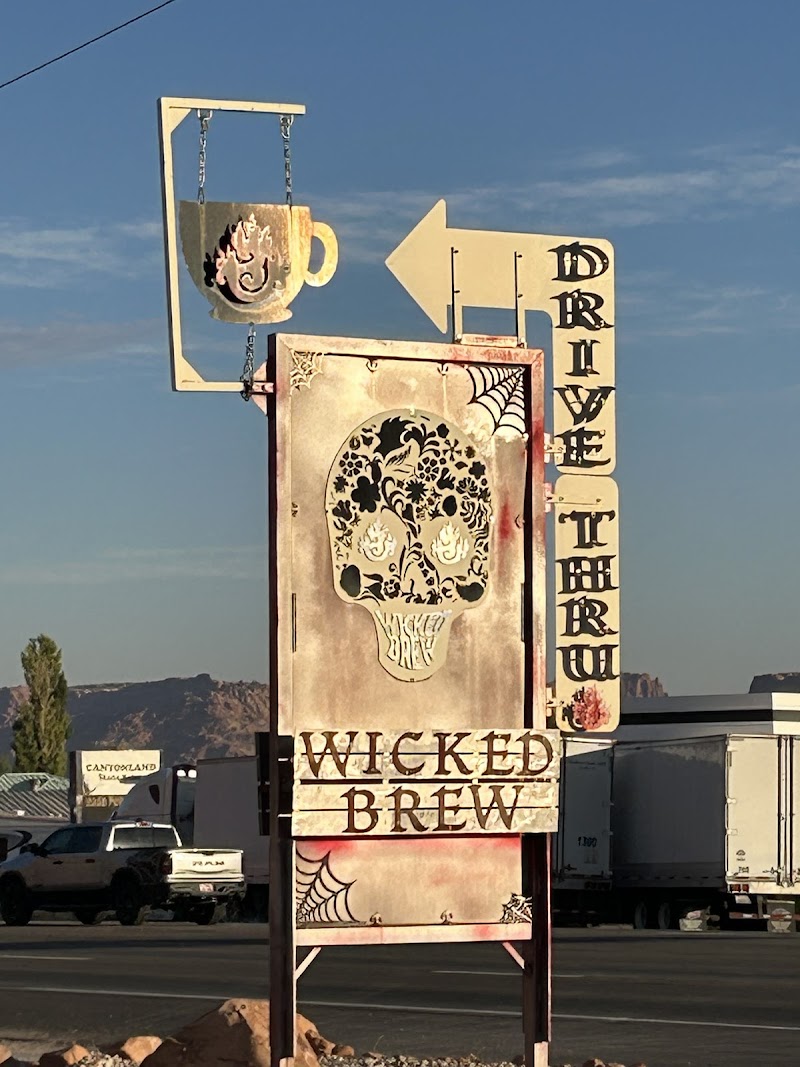 Weathered roadside drive-thru sign with a skull floral design and hanging mug, near Arches National Park.