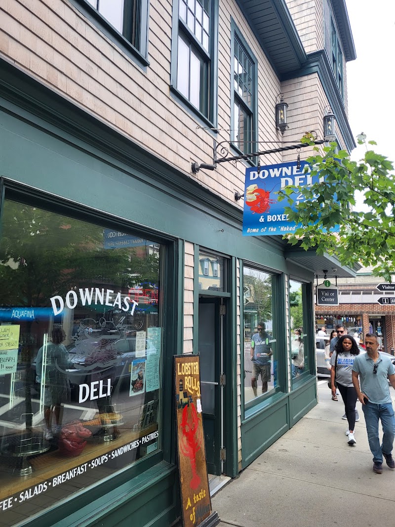 Facade of a green storefront with a blue seafood sign, large windows, and pedestrians along a brick street in Acadia National Park.