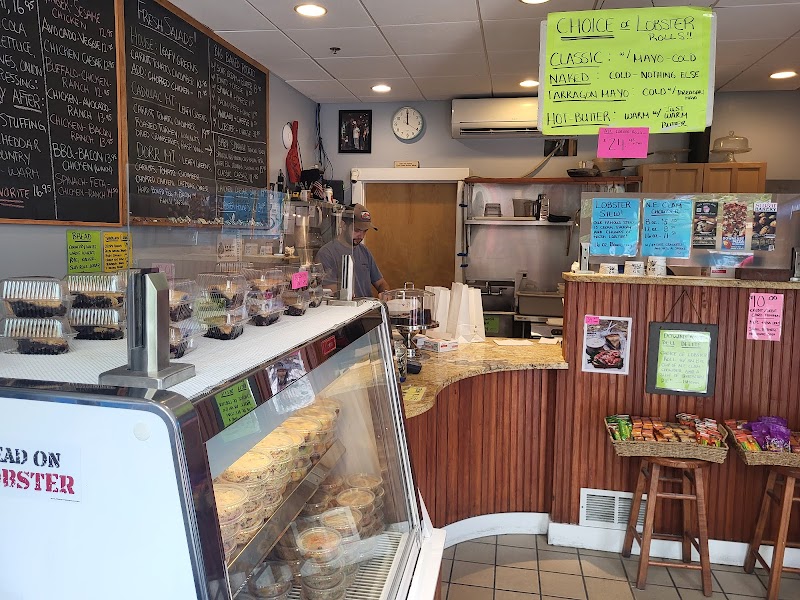 Inside a busy deli at Acadia National Park, curved wooden counter, glass pastry case, chalkboard menus overhead.