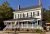 White two-story storefront with a wraparound porch, flags, and potted plants in Acadia National Park.
