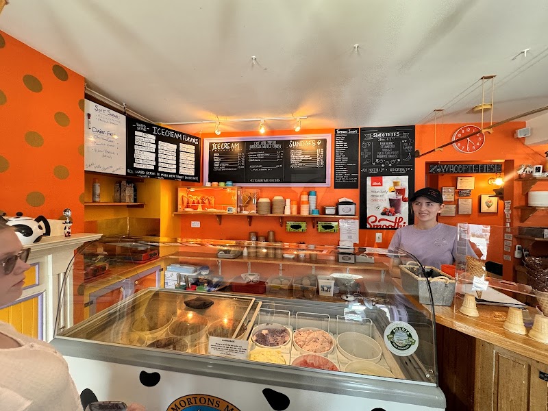 Bright orange ice cream shop interior in Acadia National Park, with a glass freezer and staff at the counter.