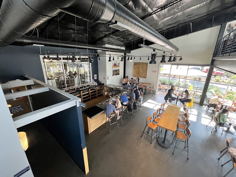 Indoor dining space with exposed ductwork, wooden tables and stools, patrons dining near large windows in Acadia National Park.