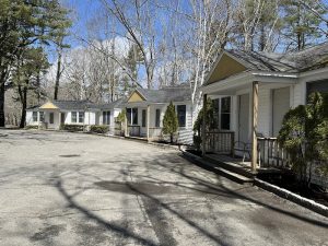 Row of white cottages with porches and yellow gables along a paved driveway in Acadia National Park, under bare trees.