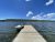 Wooden dock extends into a calm lake with a small boat tied at the end, forested hills and bright blue sky in Yellowstone National Park.