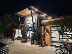 Night exterior of a wood-and-metal restaurant in Arches National Park, open doors, diners inside, bicycle outside.