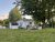 White cottage with gray trim and a large tree in Acadia National Park, with people relaxing on lawn chairs and a grill.