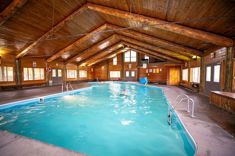 Indoor pool inside a rustic log-cabin hall with turquoise water, ladders, and windows, Yellowstone National Park.