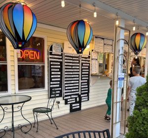 Ice cream shop storefront in Acadia National Park lit by colorful hot air balloon lanterns on a porch.