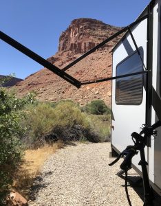 Bright blue sky over red rock formations at Arches National Park, with a camper trailer and gravel path.