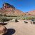 Olive tent on sandy ground beside a fire ring and picnic table, with red rock cliffs and a calm river in Arches National Park.