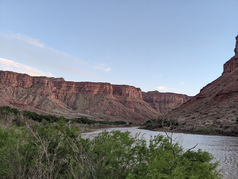 Arches National Park: red sandstone cliffs rise along a winding river with green desert shrubs and a clear blue sky.