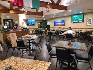 Cozy restaurant interior in Arches National Park featuring marble-topped tables, black chairs, wall TVs showing sports, and diners chatting.