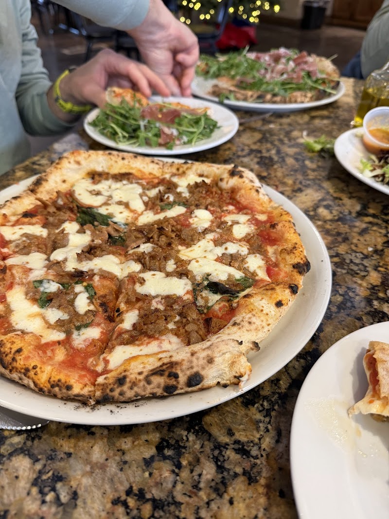Large pizza with tomato sauce, melted mozzarella, beef and basil on a white plate, with salad plates and hands reaching nearby at Arches National Park.