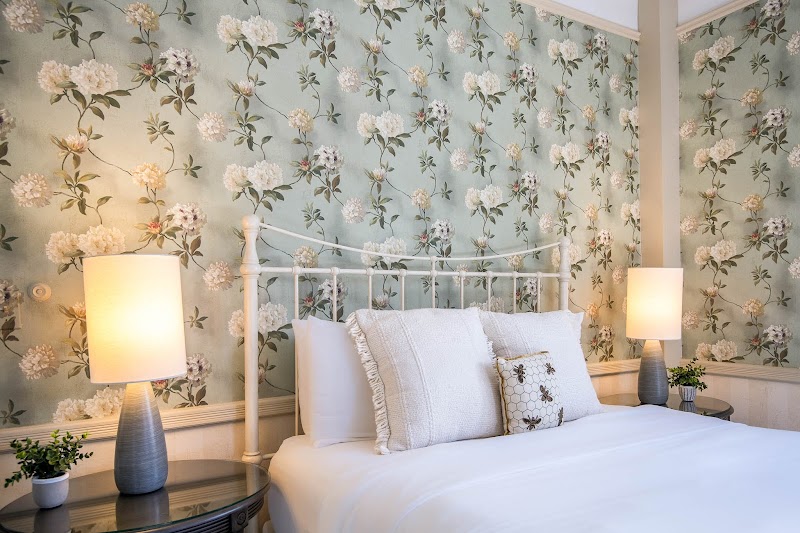 Cozy bedroom featuring a white metal bed, pastel floral wallpaper, two lamps, and potted plants in Acadia National Park.