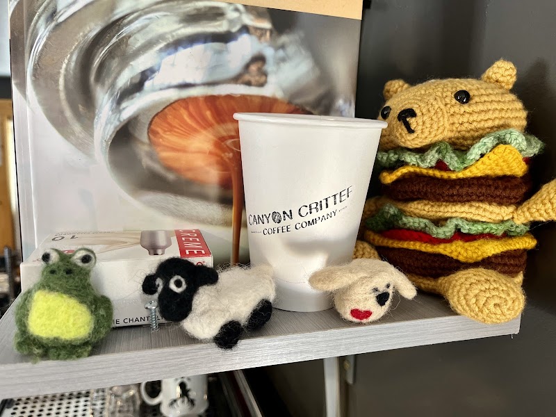 White disposable cup on a shelf beside knitted plush animals in a Glacier National Park gift shop.