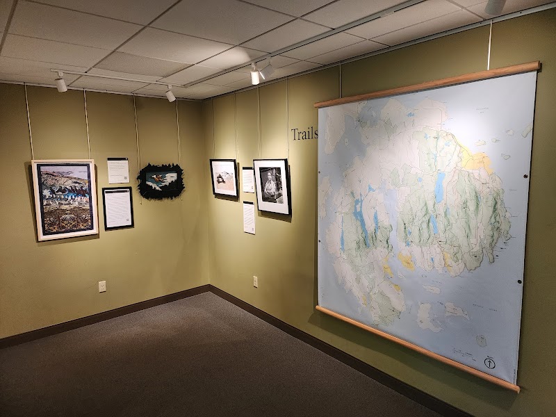 Interior of a visitor center gallery at Acadia National Park with olive walls, framed artworks, and a large wall map on the right.