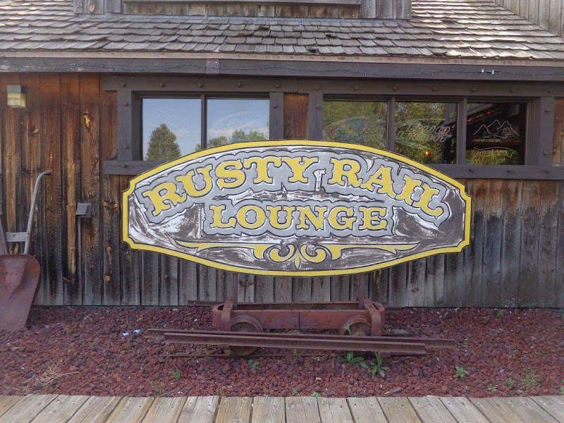 Rustic wooden building with a large curved sign in gray and yellow lettering outside, plus rusted rail wheels and a shovel, in Yellowstone National Park.