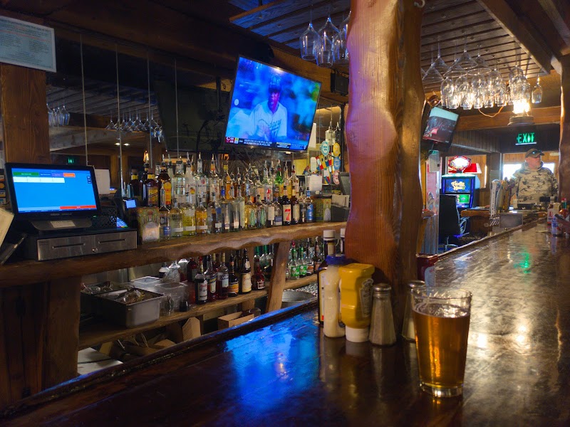 Cozy wooden bar inside a rustic lounge at Yellowstone National Park, shelves lined with liquor, a pint on the polished counter, TVs mounted above.