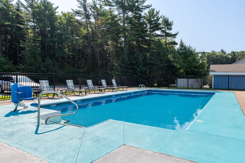 Outdoor motel-style pool with turquoise water, metal ladder, row of blue lounge chairs, and trees surrounding the area in Acadia National Park.