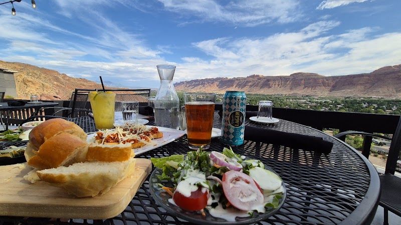 Outdoor dining on a patio at Arches National Park shows a table with bread, salad, drinks, and red rock canyon scenery.