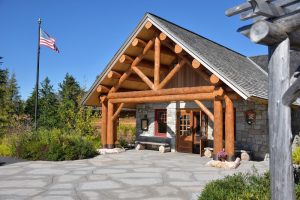 Rustic lodge-style campground entrance at Acadia National Park, near a wooded area and American flag.