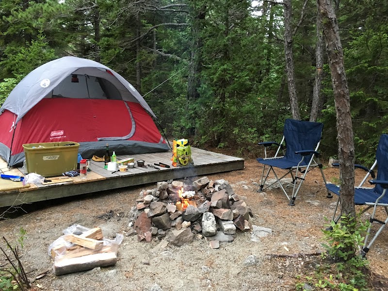 Camping setup at Quietside Campground in Acadia National Park, with a red tent on a wooden platform, campfire ring, and blue chairs nearby.