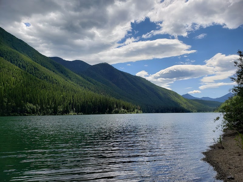 Shoreline at Harrison Lake near Glacier National Park, with forested mountains and a calm, reflective surface.