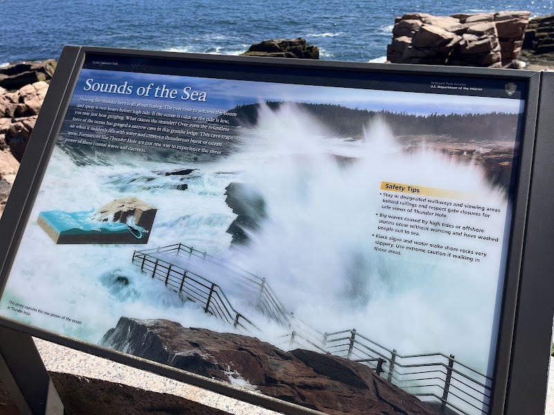 Signboard at Thunder Hole, Acadia National Park, showing crashing waves, rocky shore, railing, and safety tips.