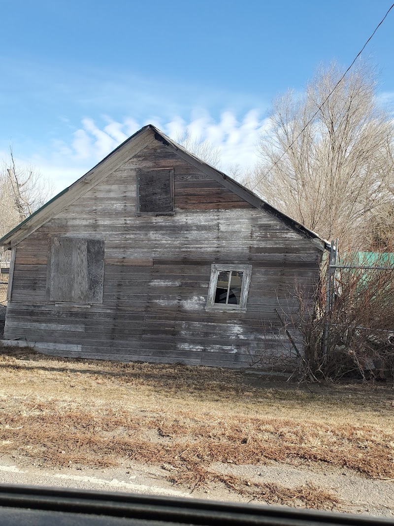 Weathered wooden cottage with boarded windows and weathered siding sits in a barren yard at Badlands National Park.
