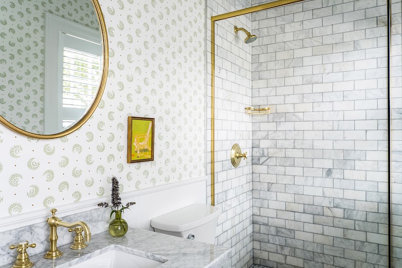 Luxurious bathroom in Acadia National Park lodging with marble countertop, brass fixtures, round mirror, and marble shower.