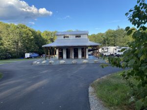 Small timber lodge with a metal roof and covered porch at Acadia National Park Hadley’s Point Campground, with RVs nearby.