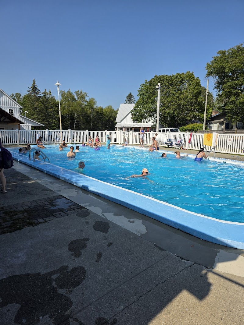 Outdoor pool at Hadley's Point Campground in Acadia National Park, with swimmers, a white fence, and blue sky.