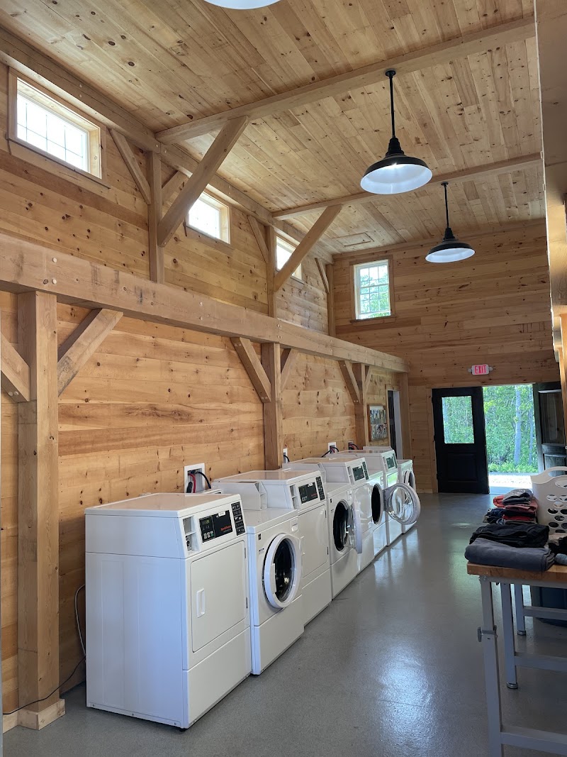 Warm wood-clad laundry room with a row of front-loading washers, exposed beams, and hanging lights in Acadia National Park campground.