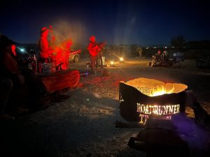 Night-time campfire gathering at Big Bend National Park campground with live music under a starry sky.
