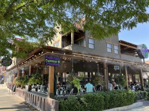 Outdoor cafe on a shaded corner with hanging plants, string lights, and patrons dining beside Arches National Park.