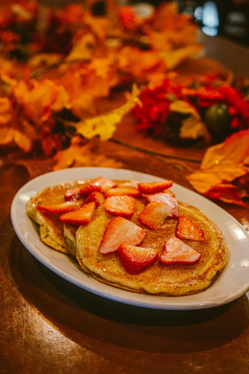Golden pancakes with strawberry slices on a white plate, warm autumn décor surrounding a restaurant table in Arches National Park.