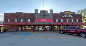 Brick storefront with a rustic wooden central facade, red awning, and a red pickup truck in the parking lot at Badlands National Park.