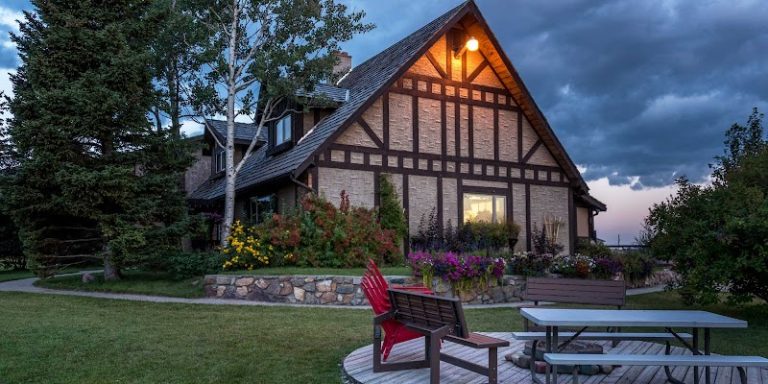 Cozy stone-and-timber lodge with flower beds, a wooden deck, red chair, and picnic table in Glacier National Park.