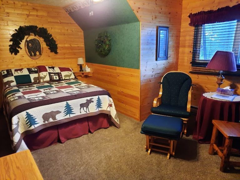 Cozy lodge bedroom in Glacier National Park with a quilted moose/tree bed, wood paneling, and a green accent wall.